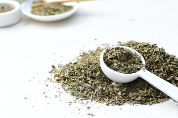 Chopped dried leaves of basil leaves on white wooden background