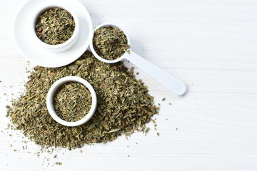 Chopped dried leaves of basil leaves on white wooden background