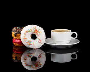 Three delicious donuts and a white coffee cup with coffee on a black background with reflection