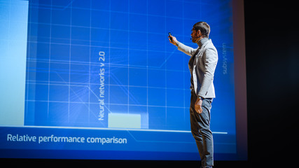 Male Speaker Stands on Stage and Does Presentation of the Technological Product, Shows...