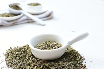 Chopped dried leaves of basil leaves on white wooden background
