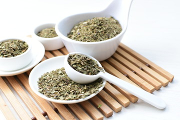 Chopped dried leaves of basil leaves on white wooden background