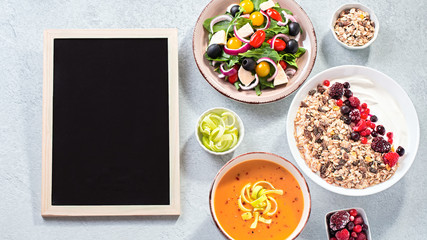 Black board fot text, assortment of dishes for dieting on concrete table top. Carrot cream soup, muesli with berries and yogurt, vegetables salad. Meal plan for diet