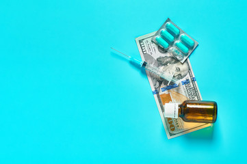 Banknote of 100 usd, capsules, bottle and syringe on green background. Corruption in medicine. Purchasing medications in pharmacy. Drugs donations. Payment for treatment. Health сare concept