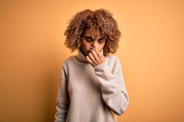 Fototapeta na wymiar Young beautiful african american woman wearing turtleneck sweater over yellow background smelling something stinky and disgusting, intolerable smell, holding breath with fingers on nose. Bad smell