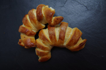 photo of fresh pastries on a beautiful dark background, like croissants, two rolls with sugar sprinkles