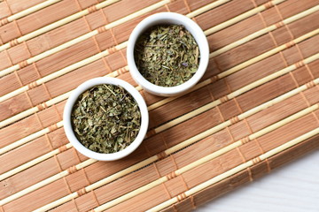 Chopped dried leaves of basil leaves on white wooden background