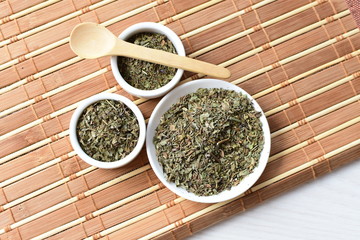 Chopped dried leaves of basil leaves on white wooden background