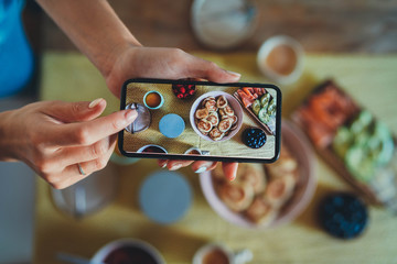 Top view image of young woman taking picture on smartphone of morning homemade breakfast with delicious pancakes, berries, avocado and salmon, close up of tasty breakfast to post in social networks