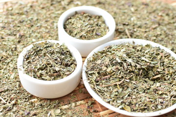 Chopped dried leaves of basil leaves on white wooden background