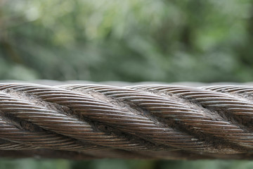 Metallic wire rope of dark color against green background 