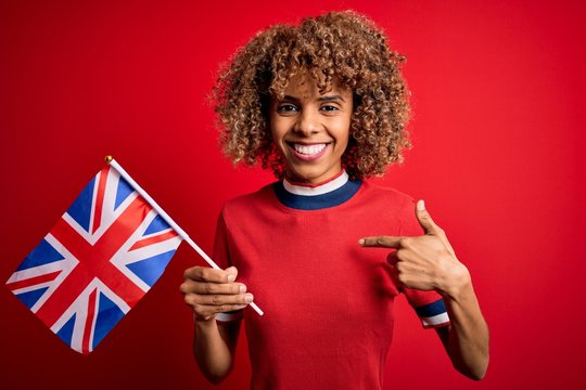 Young african american curly woman holding uk flag celebrating brexit referendum with surprise face pointing finger to himself - Powered by Adobe