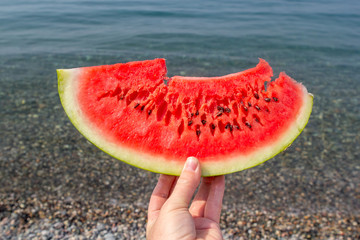 Juicy watermelon in hand on the background of the sea. Hand holding piece of watermelon on the background of sea.