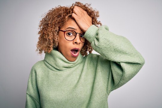 Young beautiful african american woman wearing turtleneck sweater and glasses surprised with hand on head for mistake, remember error. Forgot, bad memory concept.