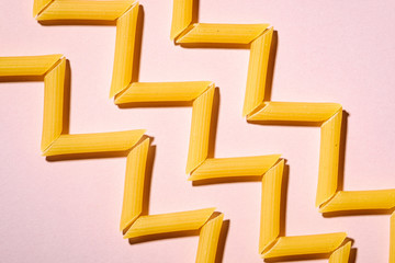 Italian pasta, raw penne tube macaroni zigzag pattern on pink background, top view, abstract food