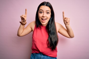 Young brunette woman wearing casual summer shirt over pink isolated background smiling amazed and surprised and pointing up with fingers and raised arms.