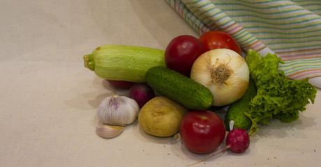 Vegetables on a wooden plate: potatoes, cucumbers, tomatoes, radishes, onions, garlic, herbs, zucchini, lettuce on a white background
