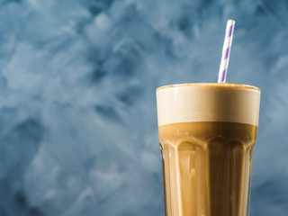 Frappe milk shake coffee in tall glass on blue and brown background. Straw