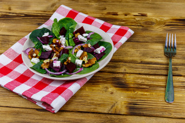 Tasty spinach salad with boiled beetroot, feta cheese, walnut and red onion on wooden table. Healthy vegetarian food
