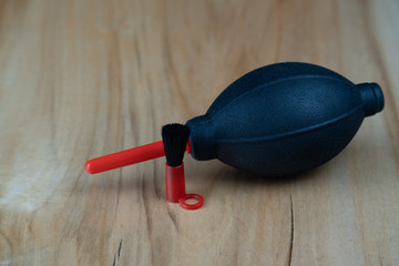 Camera cleaning kit, black and red pump and brush on a wooden table.