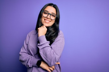 Young brunette woman wearing glasses over purple isolated background looking confident at the camera smiling with crossed arms and hand raised on chin. Thinking positive.
