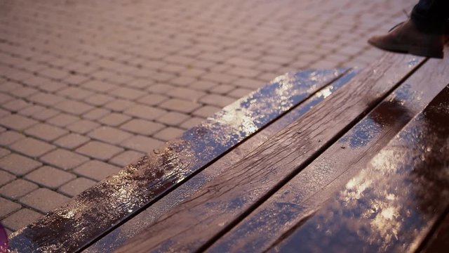 Raindrops dripping on a wooden porch, a terrace, evening reflection of lamps in drops, people walk down and up on wet boards