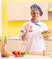 Young professional cook preparing salad at kitchen