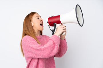 Young redhead woman with pink sweater over isolated white background shouting through a megaphone