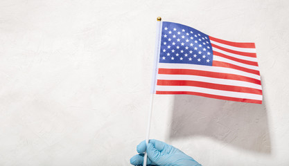 Obraz premium Hand in protecting glove holding American Flag Against White textured background. 4th of July concept. Copy space
