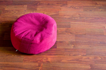 Red meditation cushion on brown wooden floor