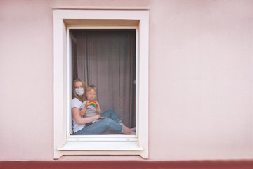 Rainbow in the window. Thank you NHS, Promotion in support of doctors in the coronavirus pandemic, covid 19. Family in the window of the house in masks and a rainbow in hands. National Health system