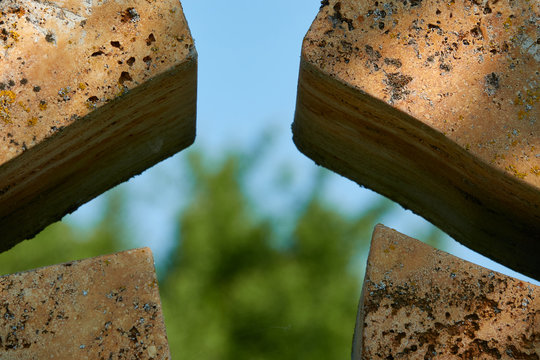 Detail of cross large and made of brown stone, religious figure carved, green nature and blue sky in the background, Germany.