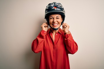 Middle age motorcyclist woman wearing motorcycle helmet over isolated white background covering ears with fingers with annoyed expression for the noise of loud music. Deaf concept.