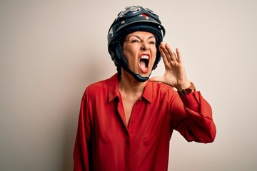 Middle age motorcyclist woman wearing motorcycle helmet over isolated white background shouting and...