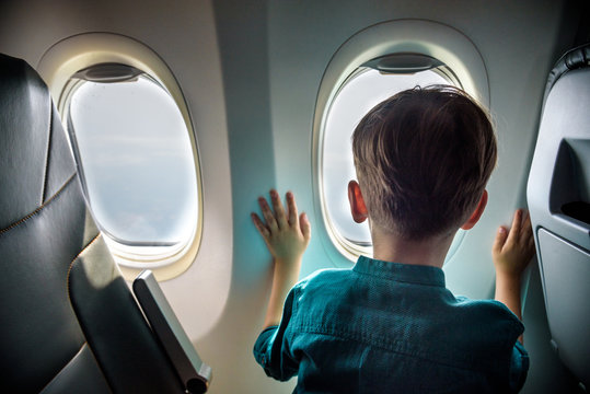 A boy have flight looking in the airplane window or porthole