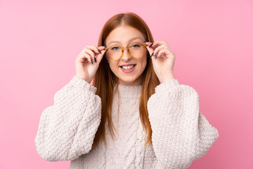 Young redhead woman over isolated pink background with glasses and surprised