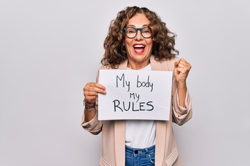 Middle age beautiful woman asking for women rights holding paper with feminist message screaming proud, celebrating victory and success very excited with raised arm