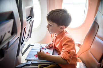 Charming kid traveling by an airplane. Joyful little boy sitting by aircraft window during the flight. Air travel with little kids © pahis
