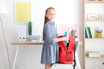 Cute cheerful schoolgirl puts stationery in a backpack. Preparation for school. Back to school. School Backpack Day
