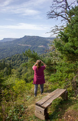 Fototapeta na wymiar a girl on the edge of a mountain looks into the distance with binoculars