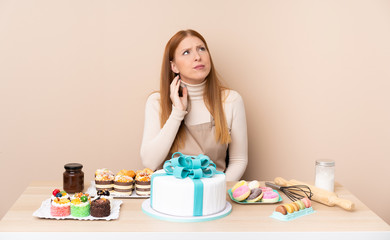 Obraz na płótnie Canvas Young redhead woman with a big cake thinking an idea