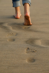 Footprints on the sand of a woman's feet, she wearing jeans trousers as she walking on the beach in low section and close up view. Vertical background concept.