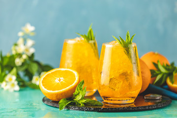Two glass of orange ice drink with fresh mint on wooden turquoise table surface. Fresh cocktail...