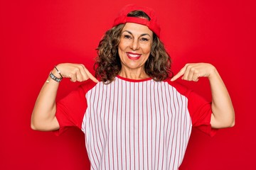 Middle age senior woman wearing baseball equiment over red isolated background looking confident with smile on face, pointing oneself with fingers proud and happy.