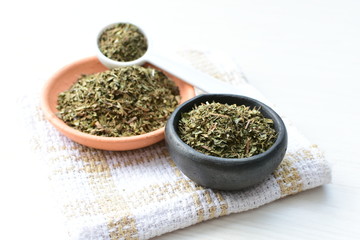 Chopped dried leaves of basil leaves on white wooden background