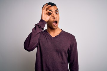 Young handsome african american man wearing casual sweater over white background doing ok gesture shocked with surprised face, eye looking through fingers. Unbelieving expression.