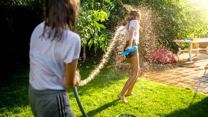 Two teenage girls playing water fight and splashing water from garden hose