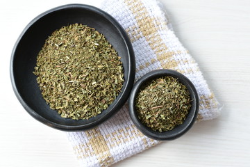 Chopped dried leaves of basil leaves on white wooden background