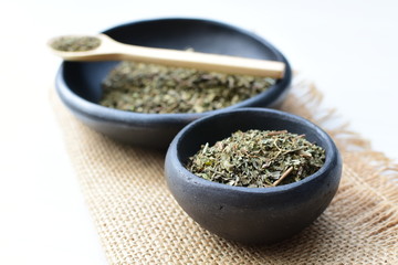 Chopped dried leaves of basil leaves on white wooden background