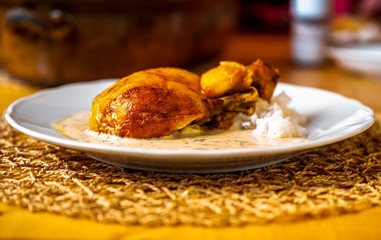 Roasted chicken leg, dill sauce and rice on plate, pan on table.